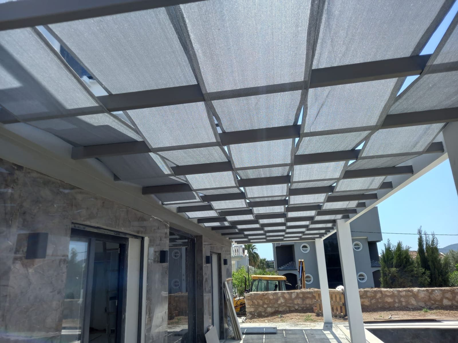 Cam görünümlü şeffaf kaplamalı geniş çelik pergolanın altından görünüm